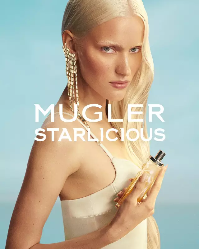 Banner della campagna Mugler Starlicious Les Eaux Gourmandes con modella in abito giallo pallido che tiene in mano il flacone di Pineapple Musk sullo sfondo di un cielo azzurro tenue.